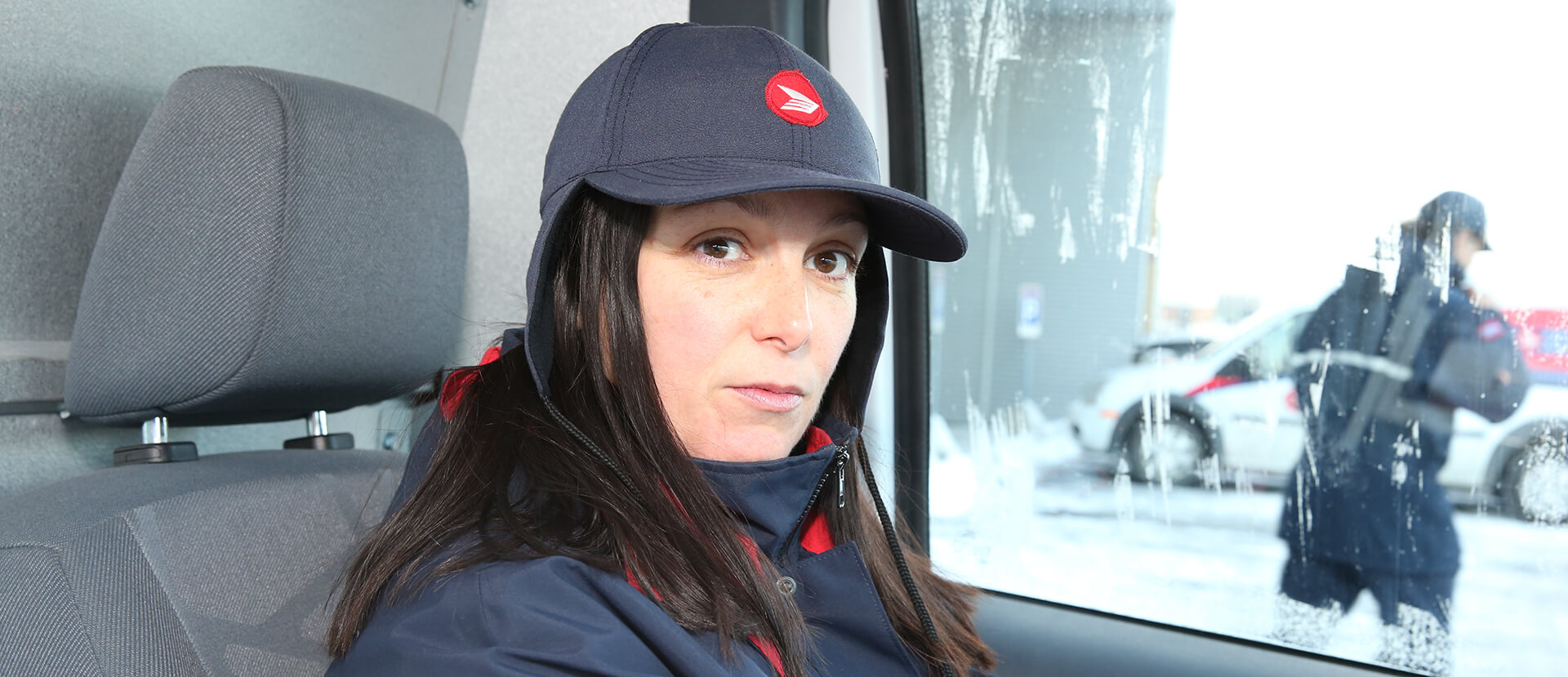 Travailleuse des postes au volant d’un camion de livraison regardant directement l’appareil photo d’un air sérieux.
